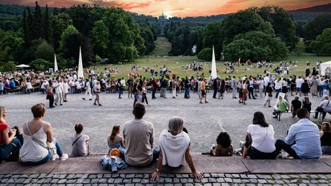 Menschen sitzen entspannt in einem Park, im Hintergrund der Herkules