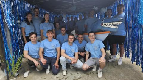 Junge Leute in blauen T-Shirts stehen um ein geschmücktes Boot 