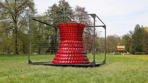 Skulptur aus roten Auto-Rücklichtern in einer blühenden Park-Umgebung