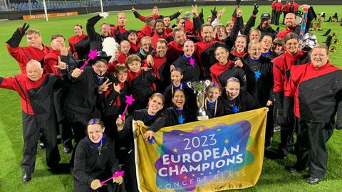 Feiernde Menschen im schwarz-roten Kostümen, vor sich ein Banner: 2023 European Champions
