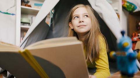 Ein Kind sitzt im Zelt und liest verträumt ein Buch