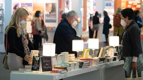 Menschen an einem Stand mit vielen Büchern und einigen Leuchten dazwischen.