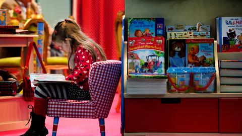 Ein Kind liest in einem Buch an einem Messestand. Das Mädchen sitzt in einem gemütlichen Sessel. 