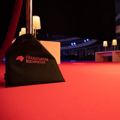 Roter Teppich in der Frankfurter Festhalle. Darauf steht ein Jutebeutel mit der Aufschrift "Frankfurter Buchmesse". 
