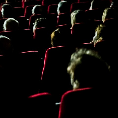Zuschauer sitzen in einem dunklen Kinosaal auf roten Sesseln.