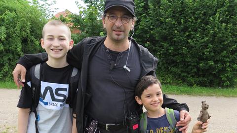 Ein Mann hält zwei kleine Jungs im Arm. Sie lächeln in die Kamera.