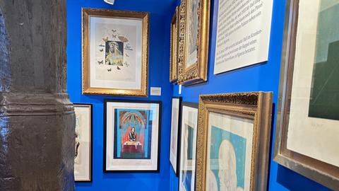Ausstellungs-Ansicht der Schau "Dali" in Steinau an der Straße. Das Bild zeigt eine blau gestrichene Wand, an der gerahmte Gemälde hängen.