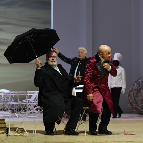 Theaterszene mit drei Männern, einer hält einen Regenschirm in der Hand