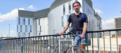 Junger Mann mit Rennrad vor einem großen, fensterlosen Gebäude.