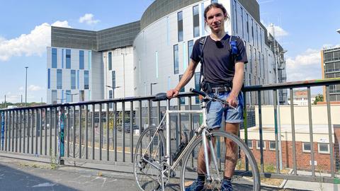 Junger Mann mit Rennrad vor einem großen, fensterlosen Gebäude.