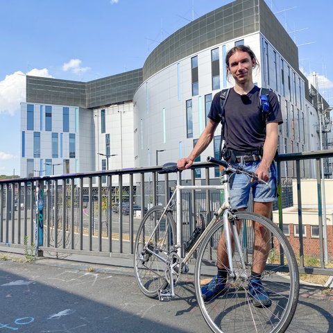 Junger Mann mit Rennrad vor einem großen, fensterlosen Gebäude.