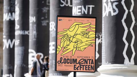 Ein Plakat der documenta in einem Plakatständer vor den Säulen des Museums Fridericianum.