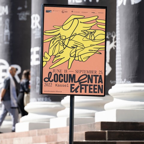 Ein Plakat der documenta in einem Plakatständer vor den Säulen des Museums Fridericianum.