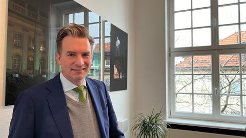 Kasseles Oberbürgermeister Sven Schoeller (Grüne) steht in seinem Büro im Rathaus, im Hintergrund ein Bild vom Friedericianum.