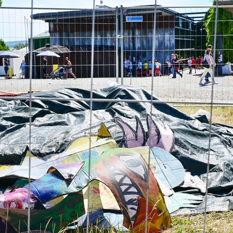 Reste einer Papp-Installation hinter einem Bauzaun. Im Hintergrund unscharf der Eingang zur documenta-Halle und Besucher davor.