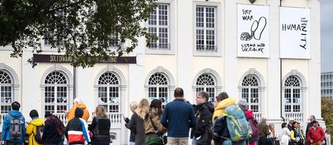 Besucherschlange vor dem Ausstellungsort Fridericianum, an dessen Außenwand Kunstwerke zu sehen sind.