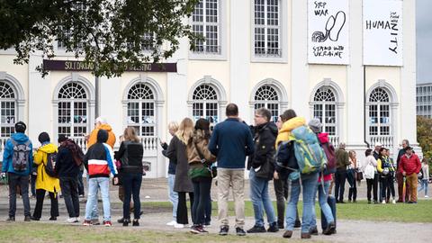 Besucherschlange vor dem Ausstellungsort Fridericianum, an dessen Außenwand Kunstwerke zu sehen sind.