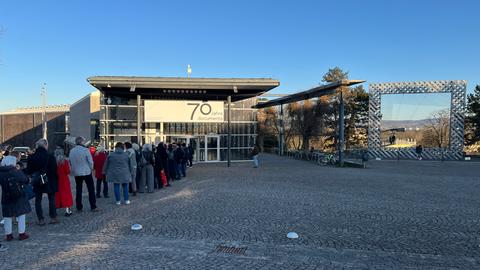 vor EinemGrobengeBäudemit -Glasfassade Steht Ein Menschenschlange