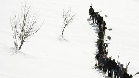Filmausschnitt: Eine Gruppe von Männern mit Spaten stapft durch eine Schnee-Landschaft