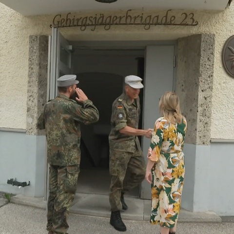Eine Frau im Blumenkleid schüttelt einem Soldaten in Uniform die Hand