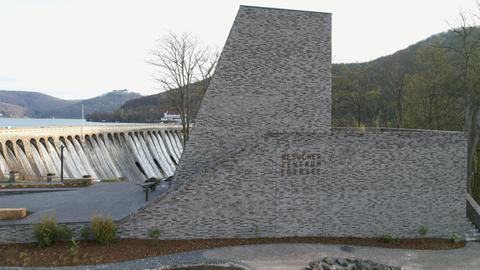 Außenansicht des Besucherzentrums Edersee, ein Ziegelbau, im Hintergrund die überlaufende Staumauer.