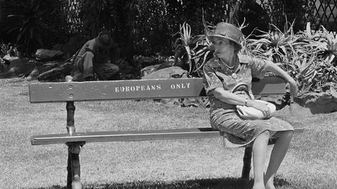 Frau sitzt auf einer Bank mit der Aufschrift "Europeans Only"