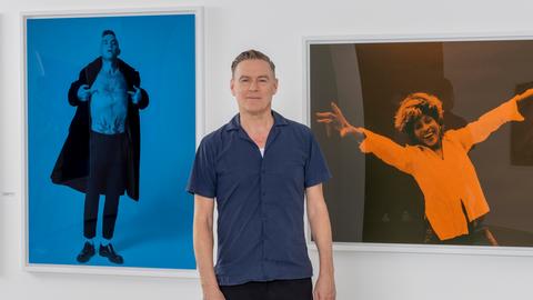 Ein Mann steht vor einer Wand, an der drei Bilder hängen.