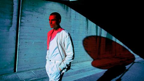 Ein männliches Model läuft an einer Betonwand entlang - sein Gesicht wird mit rotem Licht beleuchtet. 