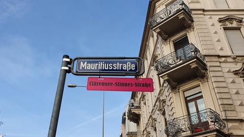 Unter einem blauen Schild mit der Aufschrift "Mauritiusstraße" hängt ein rotes Schild mit der Aufschrift "Clärenore-Sinnes-Straße".