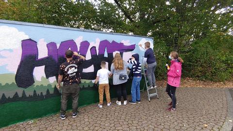 Kinder und Jugendliche besprühen eine wand mit Graffiti.