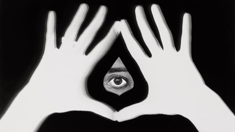 Arbeit von Esther Ferrer, Manos feministas, 1977 Zwei Hände formen mit Daumen und Zeigefinger eine Vulva vor schwarzem Hintergrund - ein Auge schaut heraus.