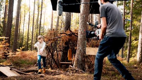 Ein Kameramann filmt ein weglaufendes Kind im Wald.