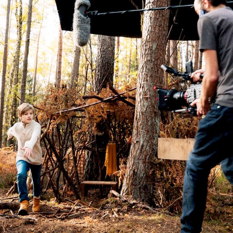 Ein Kameramann filmt ein weglaufendes Kind im Wald.
