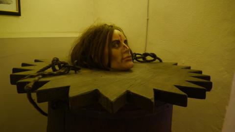 Das Bild zeigt ein Ausstellungsstück des Foltermuseums Rüdesheim: ein gezacktes Rad, aus dem ein Kopf herausschaut.