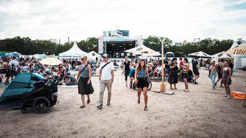 Das Bild zeigt Menschen, die auf dem Festivalgelände zwischen Zelten auf dem Boden sitzen.