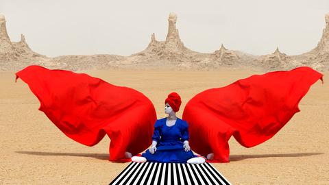 Eine Frau mit roten Stoffflügeln sitzt in der Wüste