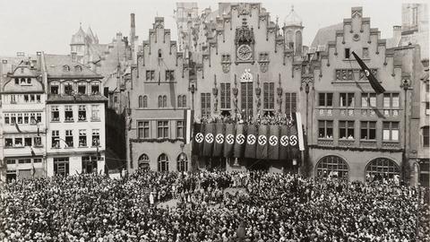 Ausstellung "Frankfurt und der NS", Schwarzweiß-Bild des Römerbergs, auf dem sich eine Menschenmasse versammelt hat, am Rathaus hängen Hakenkreuzfahnen