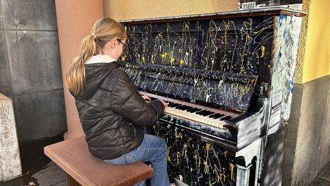 Eine junge Frau spielt an einem Klavier im Freien, das mit Farbspritzern übersät ist.