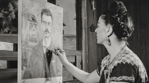 Frida Kahlo sitzt malend an einer Staffelei.