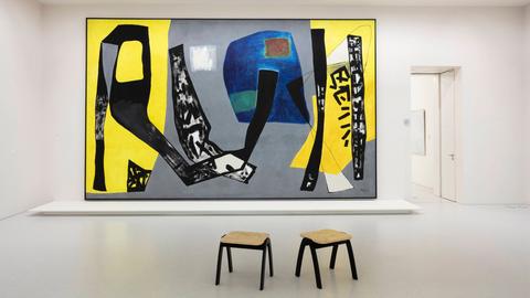 Fritz Winter, Komposition vor Blau und Gelb, großformatiges Gemälde in einer Ausstellungshalle, davor stehen zwei Hocker