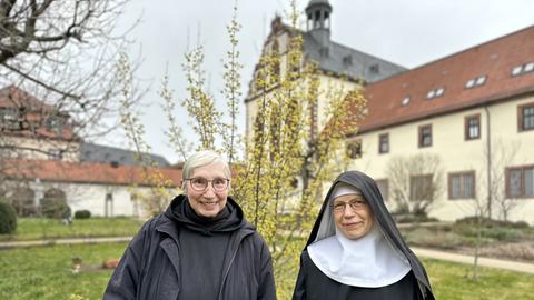Zwei Frauen im Klostergarten, eine trägt eine Schwesternhaube.