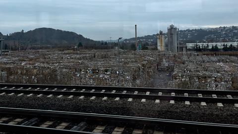 Blick aus einem Zugfenster auf ein Industriegelände mit großen Papierballen