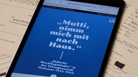 Handy mit einem blauen Hintergrund mit der Inschrift zur Ausstellung "Mutti, nimm mich mit nach Haus"