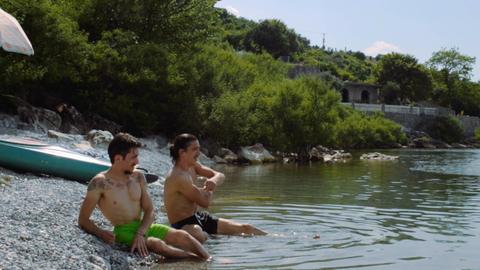 Zwei junge Männer in Badekleidung an einem See-Ufer