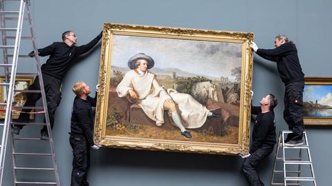Das Gemälde "Goethe in der römischen Campagna" wird von vier Männern an seinen neuen Platz im Sammlungsbereich gehängt. 