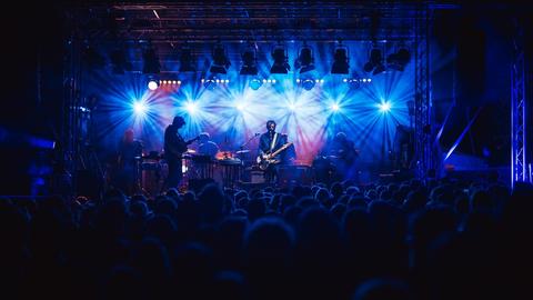 Menschen stehen vor einer Bühne, auf der eine Band auftritt