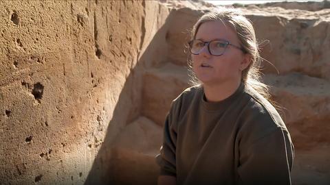 Eine junge Frau mit Brille sitzt in der Grube und schaut den Betrachter an.