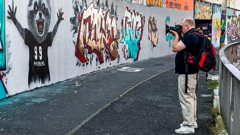Ein Mann mit Rucksack fotografiert Graffiti an einer Wand