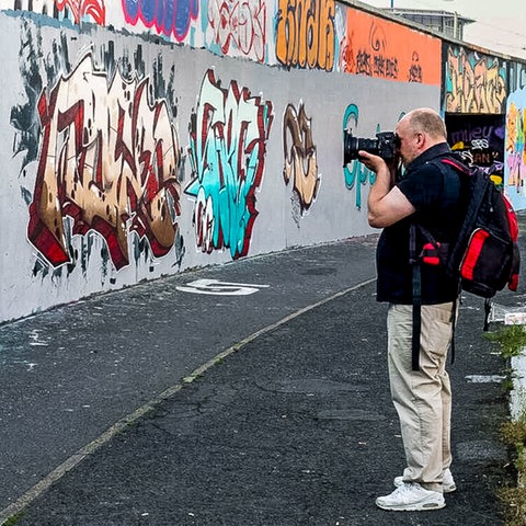 Ein Mann mit Rucksack fotografiert Graffiti an einer Wand