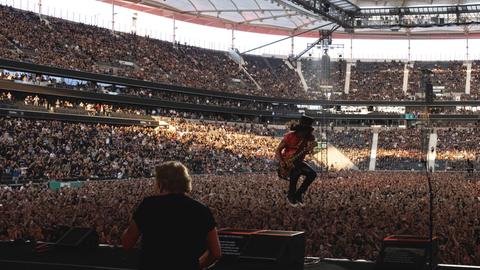 Ein Mann mit Gitarre springt auf einer Bühne von einer Box.